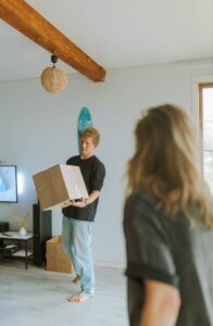 A couple carrying moving boxes into a new home to show the sentiment of buying into the housing market in Denver