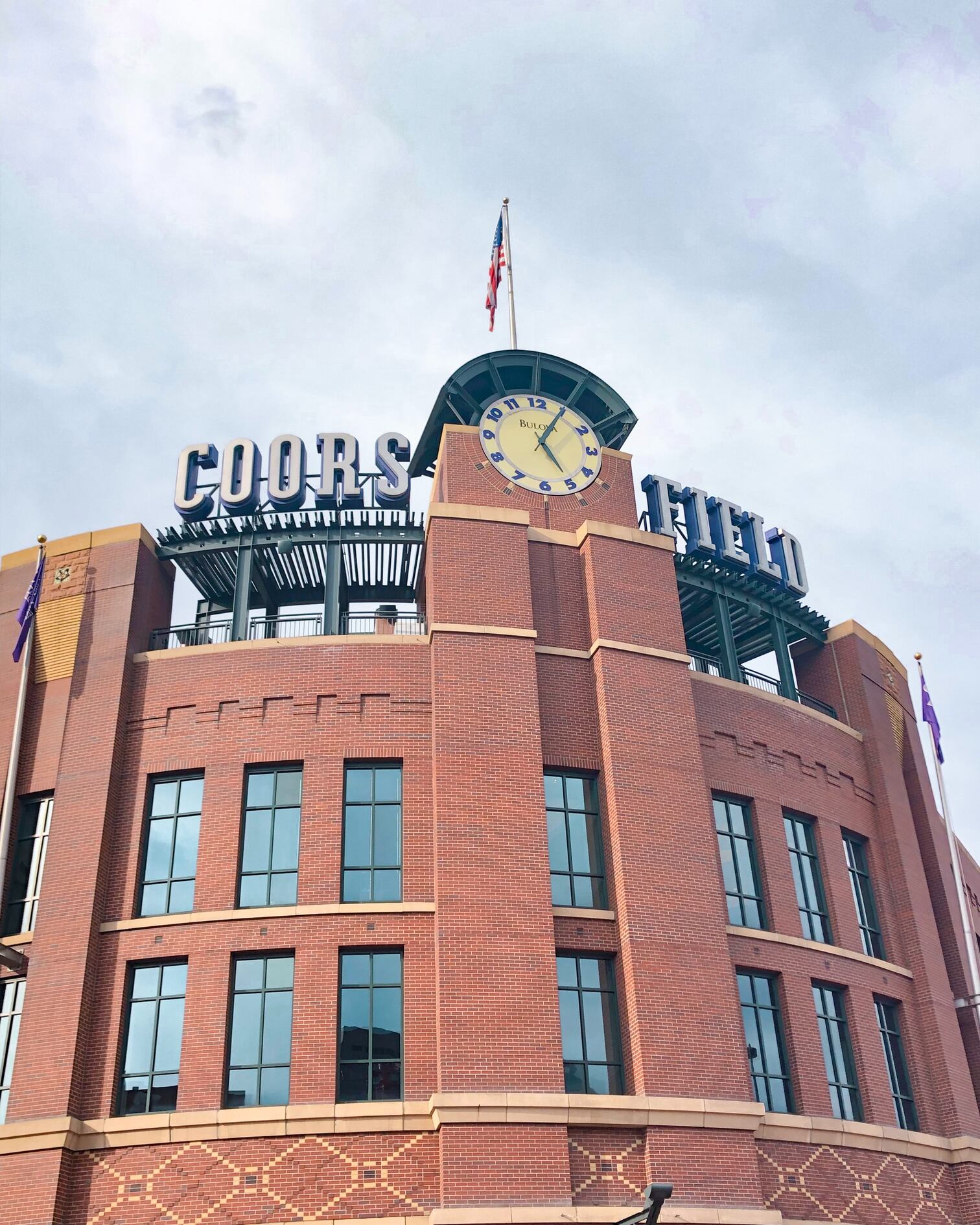Coors Field baseball stadium near Barclay downtown Denver condos is brick with windows, a large clock, and a flag.