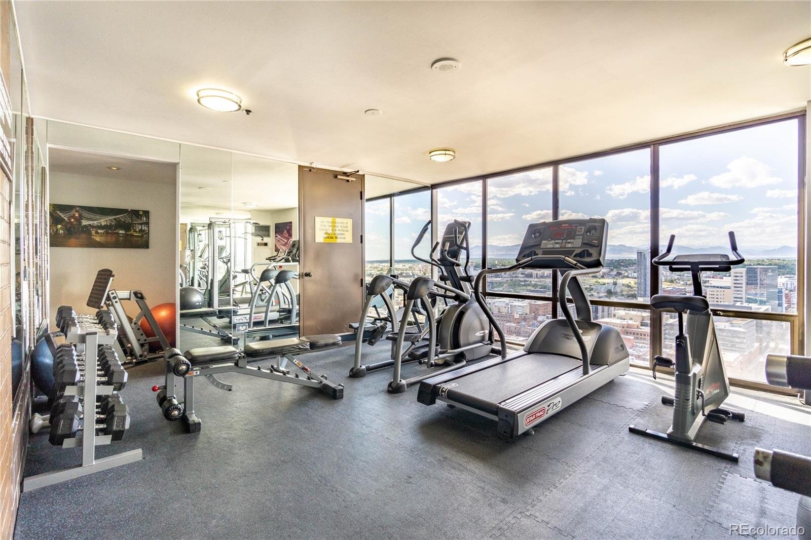 The gym at the Barclay downtown Denver condos with equipment facing city views through floor to ceiling windows.